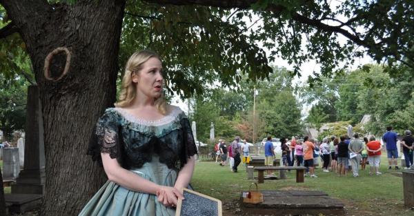Costumed interpreter at a living history event with visitors in the background in Huntsville
