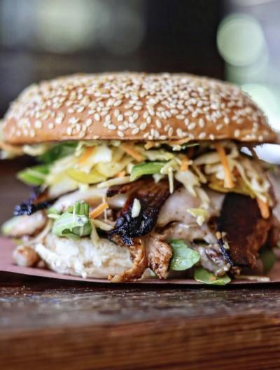 Close-up of a barbecue sandwich from Blue Oak BBQ topped with smoked meat, crunchy slaw, and green onions on a sesame seed bun.