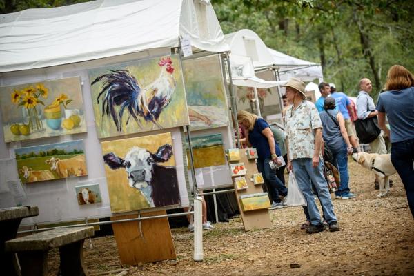 Visitors browse paintings and handmade artwork at an outdoor art festival with white tents in Huntsville.