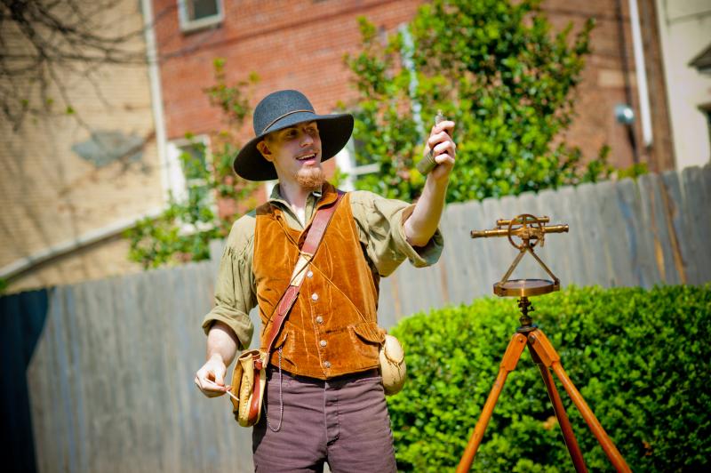 Historical reenactor demonstrating 19th-century surveying tools at a living history site in Huntsville