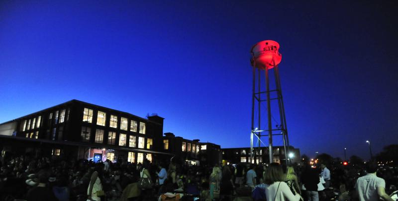 Crowd gathered at night near a glowing water tower during an outdoor event in Huntsville