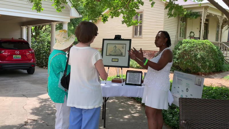 Outdoor history demonstration with visitors gathered around an exhibit table in Huntsville