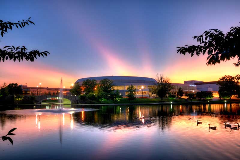 Von Braun Civic Center lakeside fountain at sunset with trees and vibrant hues reflecting on water